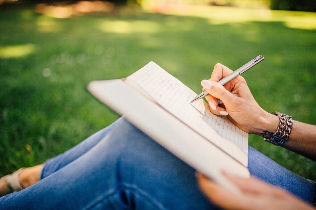 Person writing in a notebook while sitting outdoors.