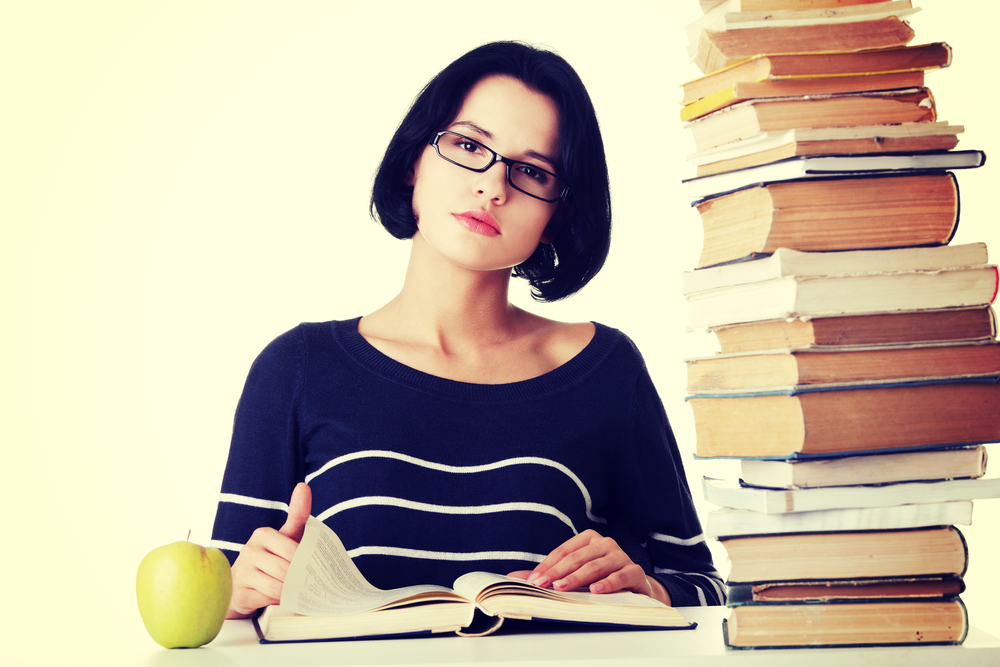 Woman studying with books and an apple on the desk.
